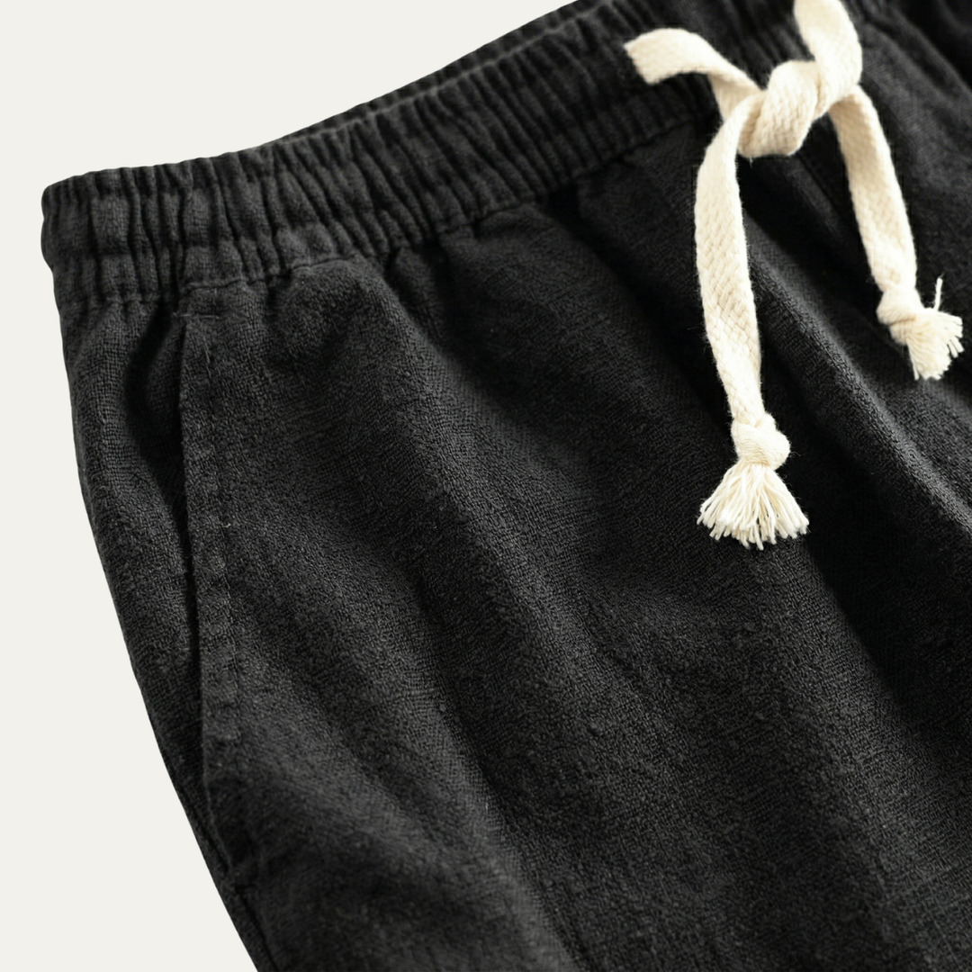 Black linen beach shorts with elastic waist and cream drawstring, close-up detail
