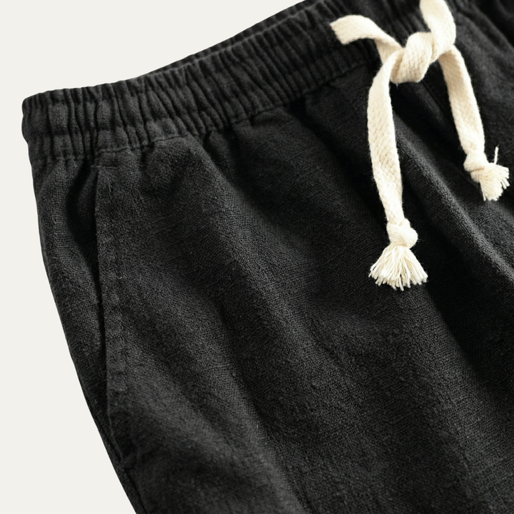 Black linen beach shorts with elastic waist and cream drawstring, close-up detail