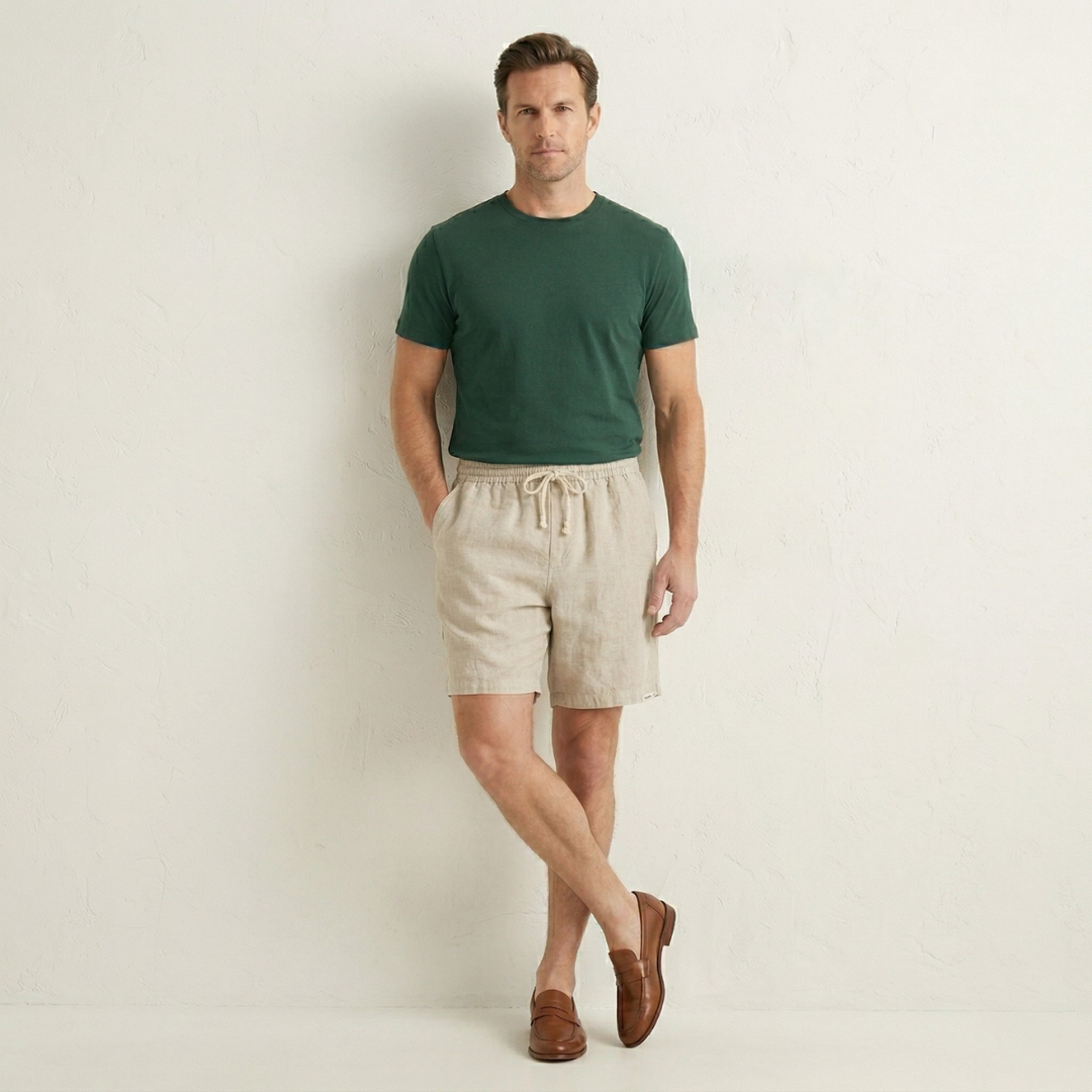 Men beige linen beach shorts worn with green t shirt and loafers, studio shot