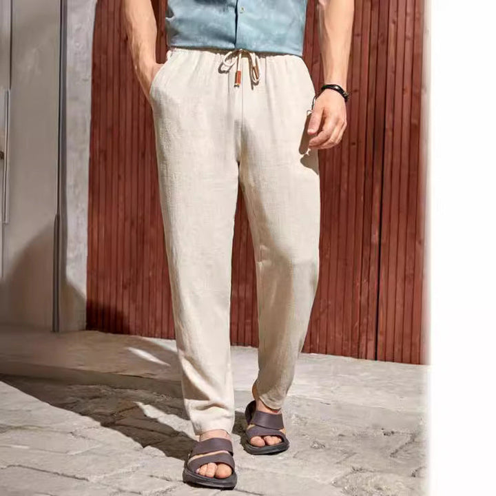 Men linen pants in beige with relaxed straight leg and drawstring waist, styled with sandals