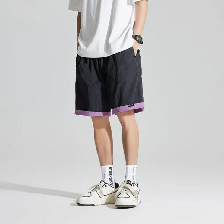 Front view of black reversible casual shorts with purple cuffed hem, styled with sneakers and socks