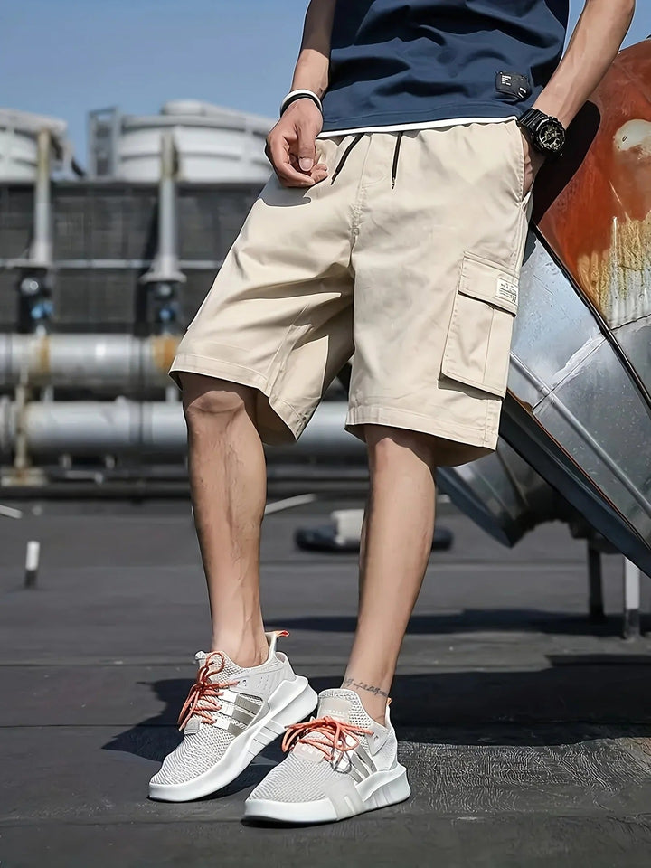 Beige men cargo shorts with large side pocket and drawstring waist, paired with white athletic shoes