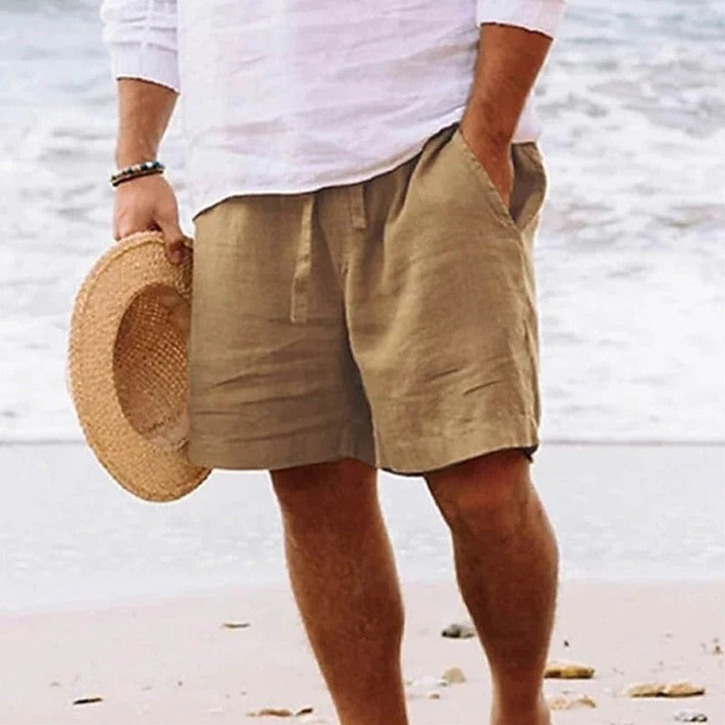 Beige knee length linen shorts with drawstring waist and side pockets on a man at the beach