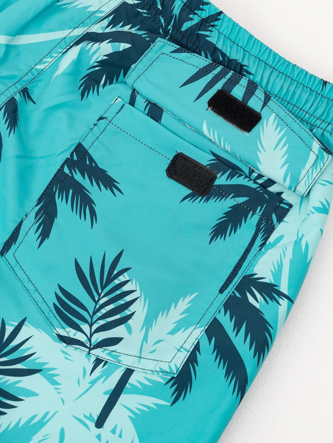 Close-up of men's beach swim shorts showing palm print, side pocket, and back flap pocket details