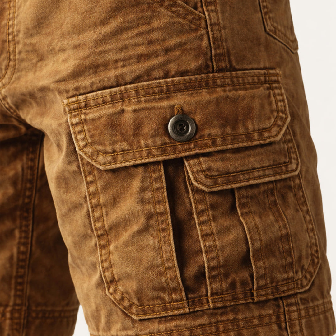 Close-up of tan cargo shorts side pocket with button flap and reinforced utility stitching
