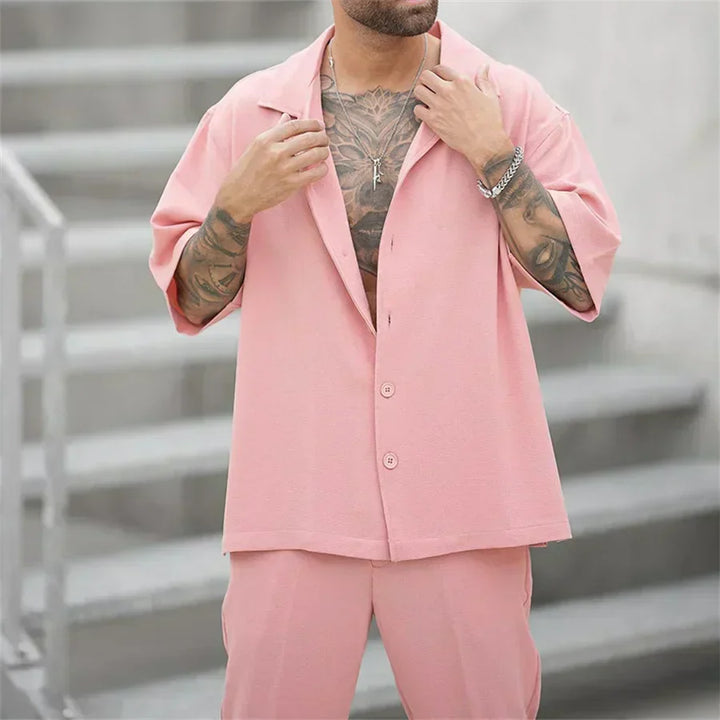Close-up of pink short sleeve button shirt and matching pants set on a man with tattoos
