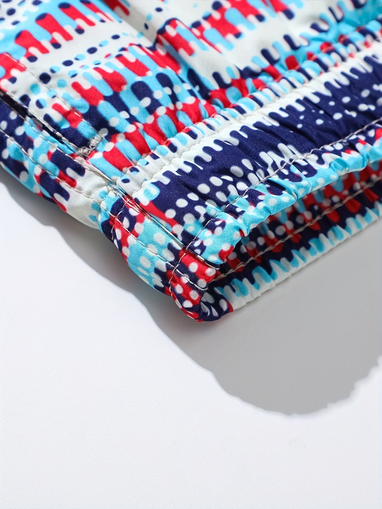 Close-up of men's swim shorts hem showing stitched seam and bold blue red navy graphic print