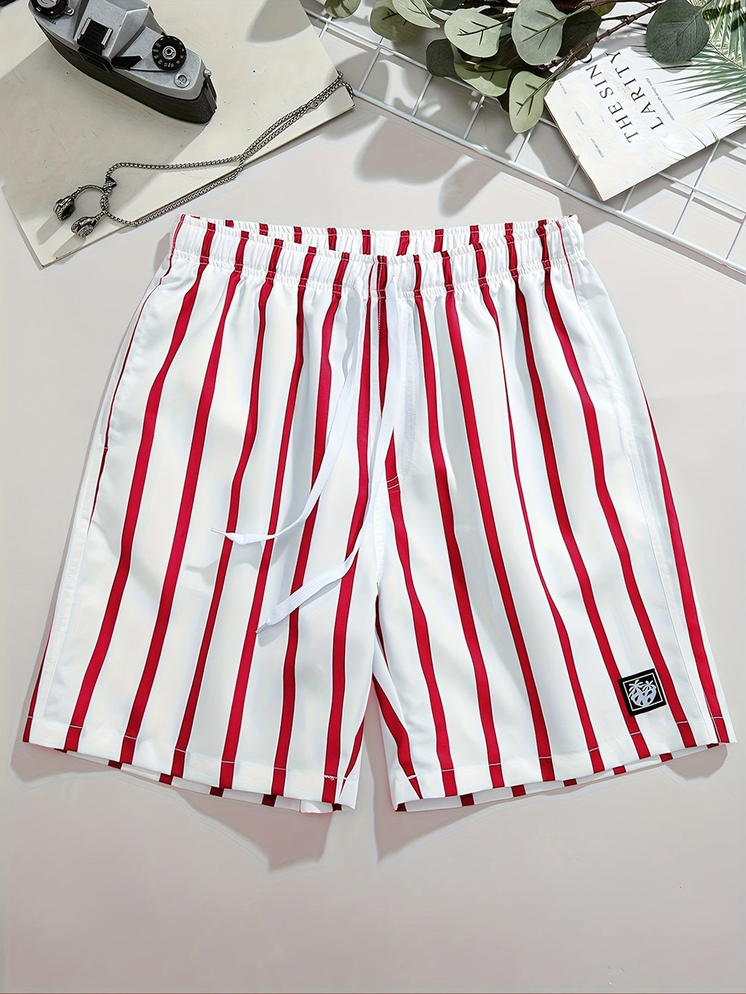 Men's white swim shorts with red vertical stripes, drawstring waist, and logo patch