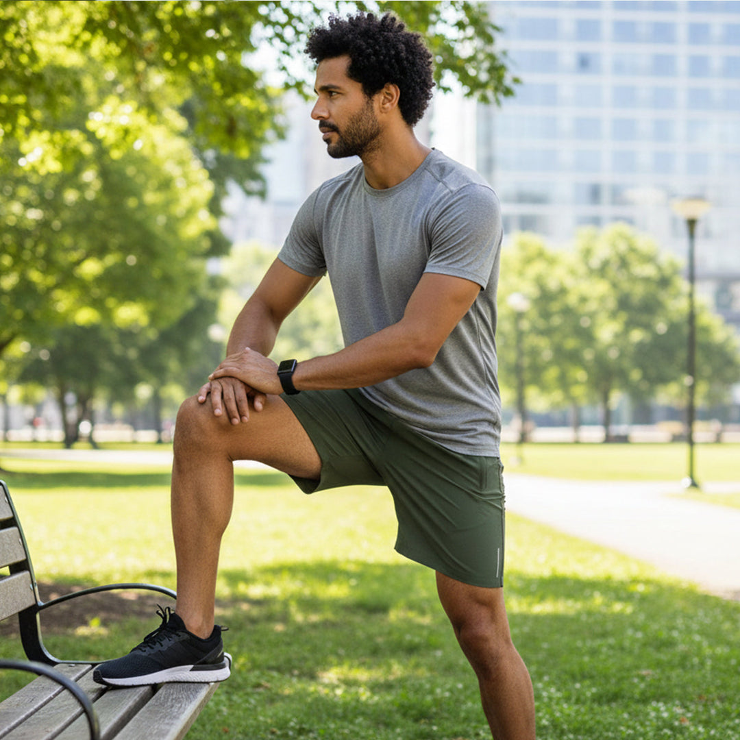Man in olive green running shorts with pockets stretching in a park