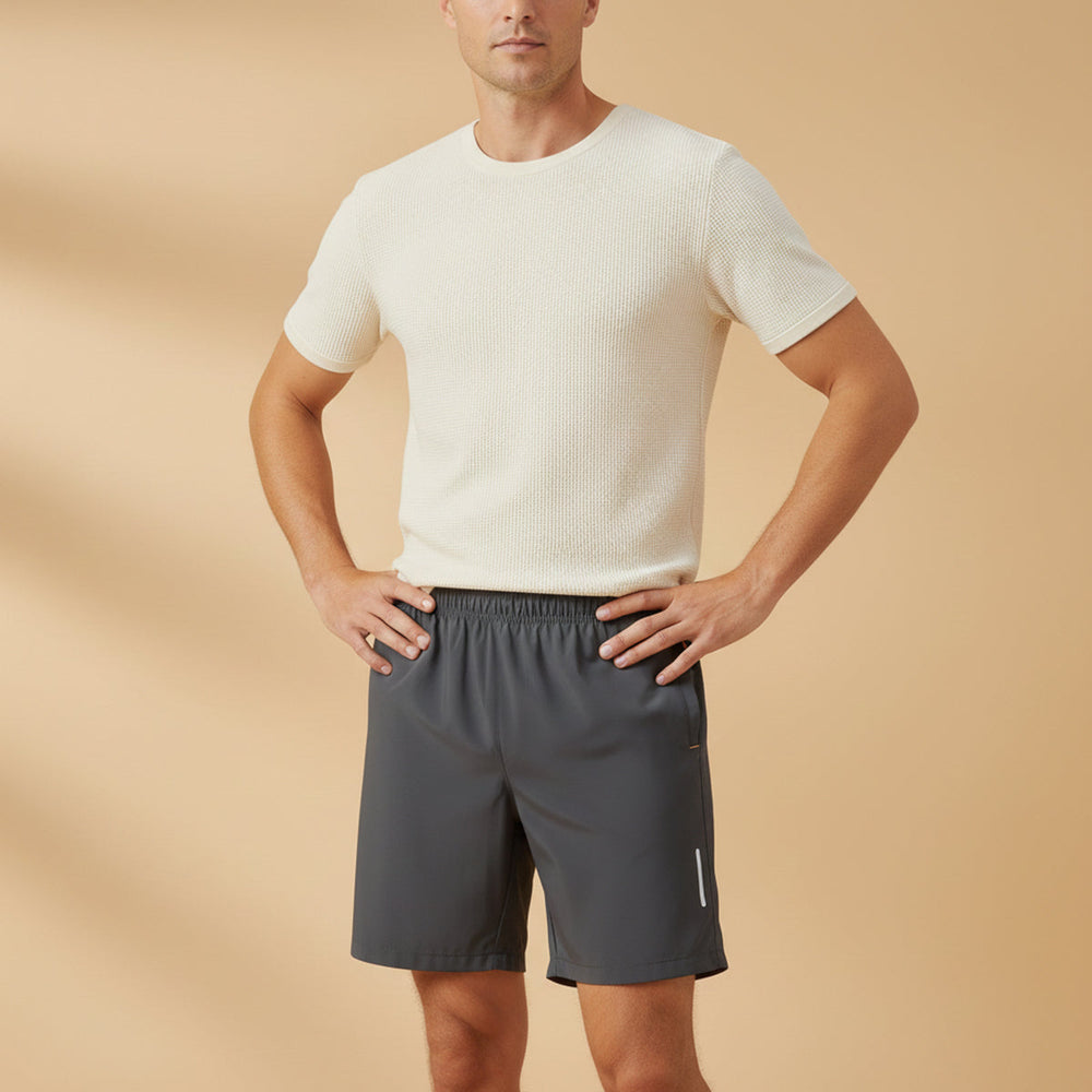 Model wearing dark gray men's lightweight running shorts with pockets and reflective details