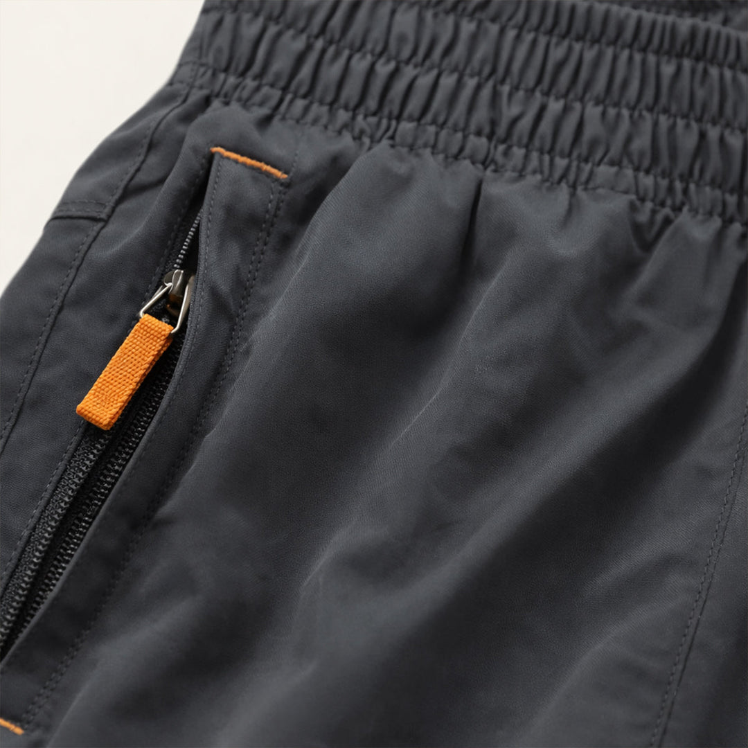 Close-up of dark gray running shorts pocket with orange zipper pull and elastic waistband