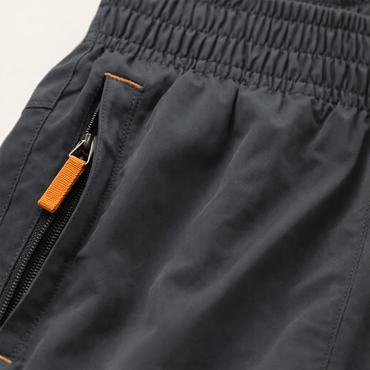 Close-up of dark gray running shorts pocket with orange zipper pull and elastic waistband
