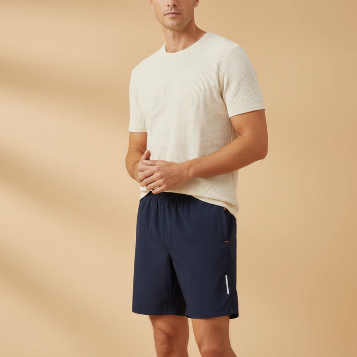 Model wearing navy blue men's lightweight athletic shorts with pockets and reflective detail
