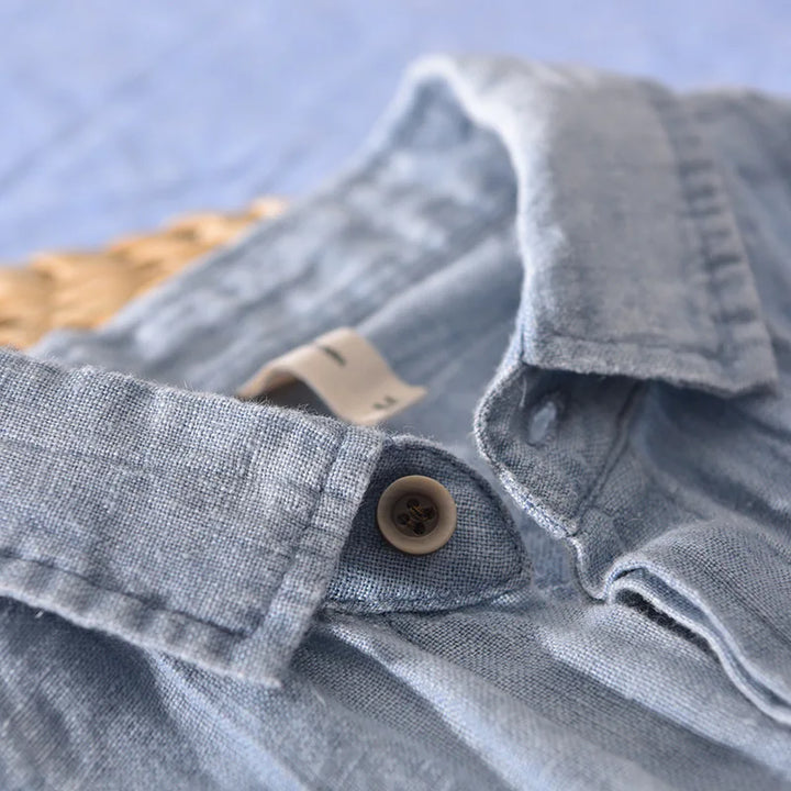 Close-up of light blue linen shirt collar and button detail with textured fabric