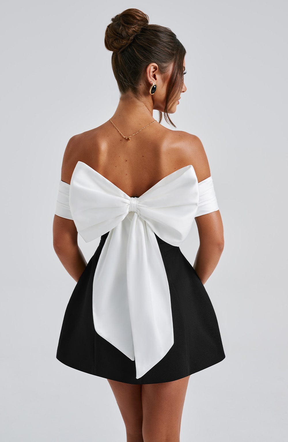 Back view of black cocktail mini dress with oversized white bow and off shoulder sleeves