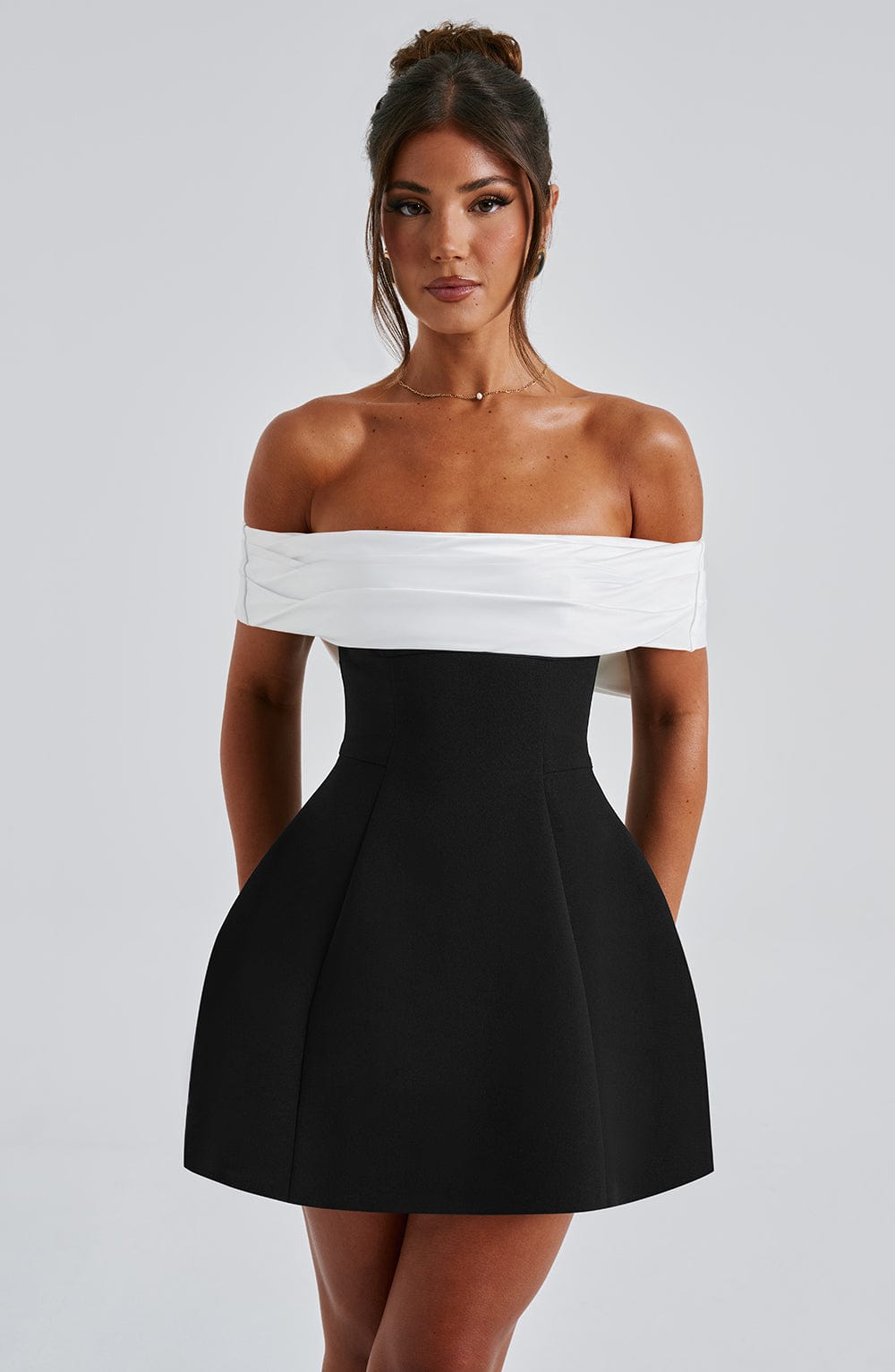 Front view of off shoulder mini dress with white draped neckline and structured black skirt