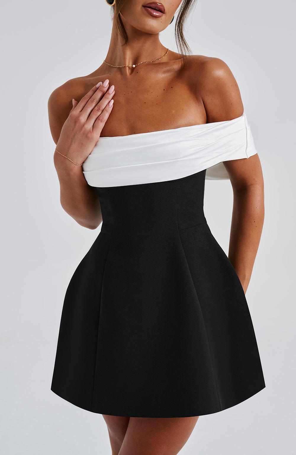Close front view of black mini dress showing white off shoulder wrap detail and fitted waist