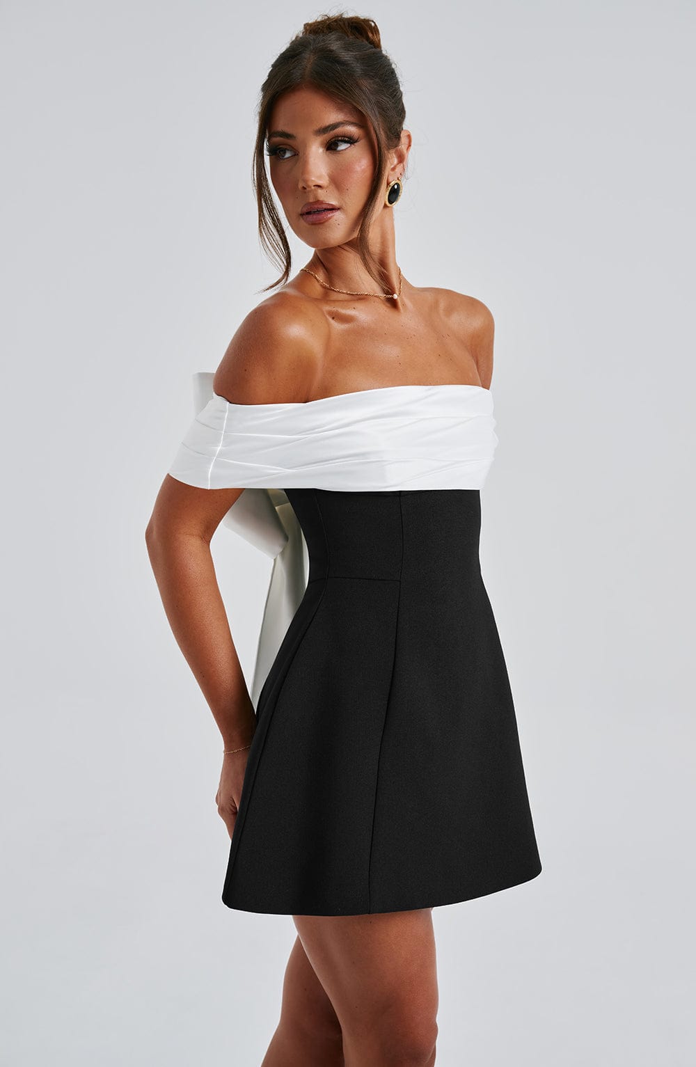 Side view of black cocktail dress with white off shoulder neckline and flared mini skirt