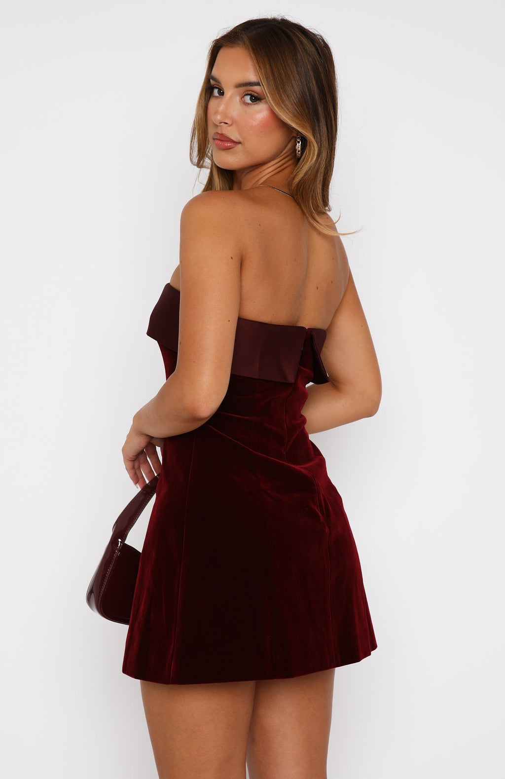 Back three-quarter view of burgundy strapless velvet mini dress highlighting straight back