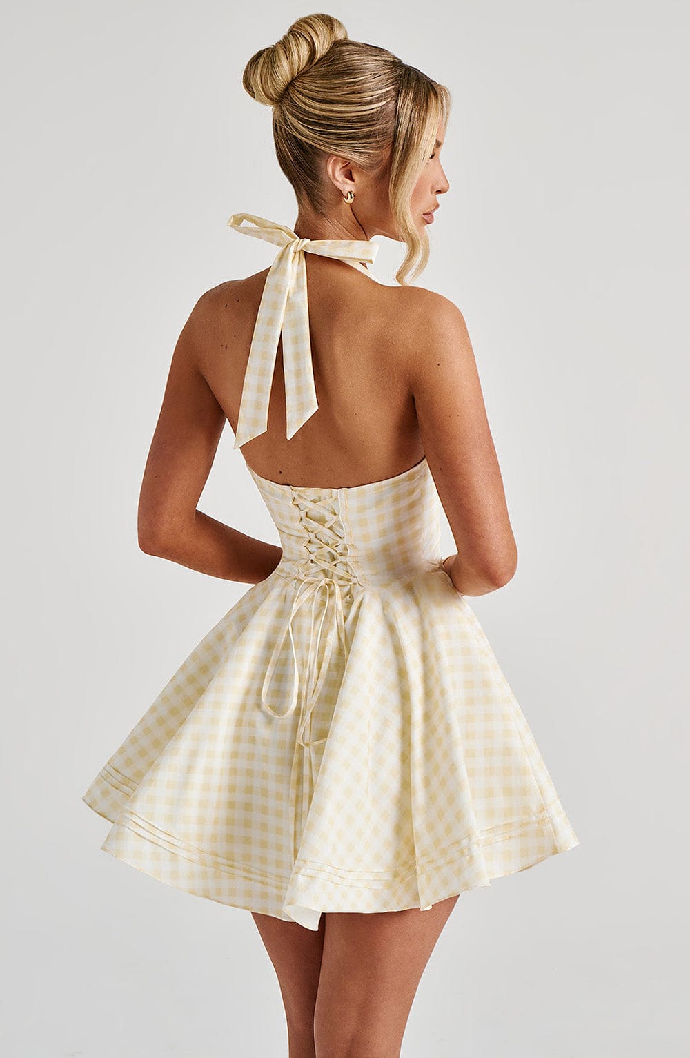 Back view yellow gingham halter mini dress with tie neck and lace-up corset back, flared skirt