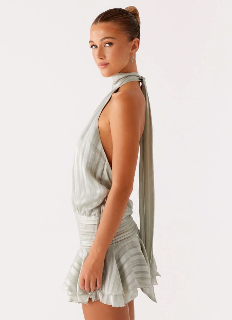 Side profile of light blue halter mini dress showing open back and flowing tie detail