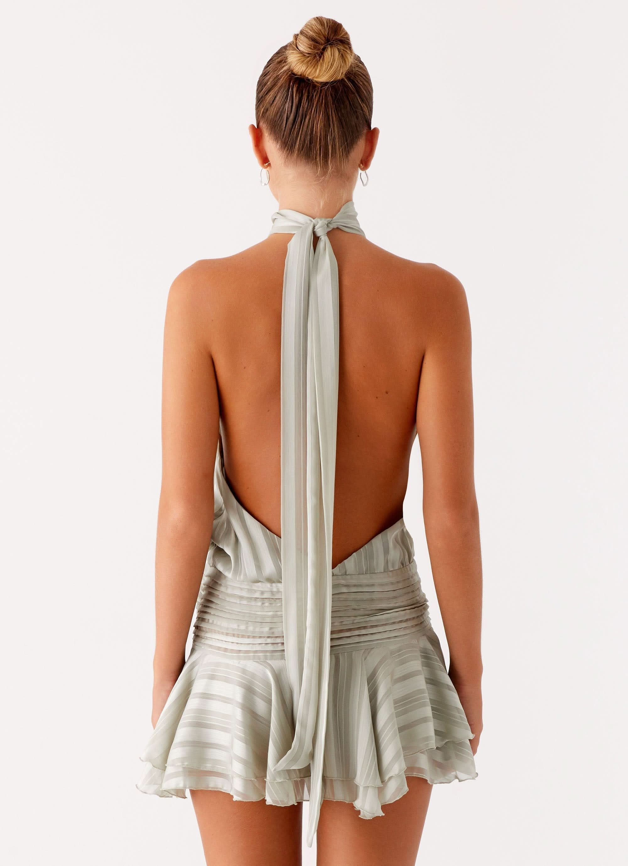 Back view of sage green halter mini dress with deep open back and long neck tie