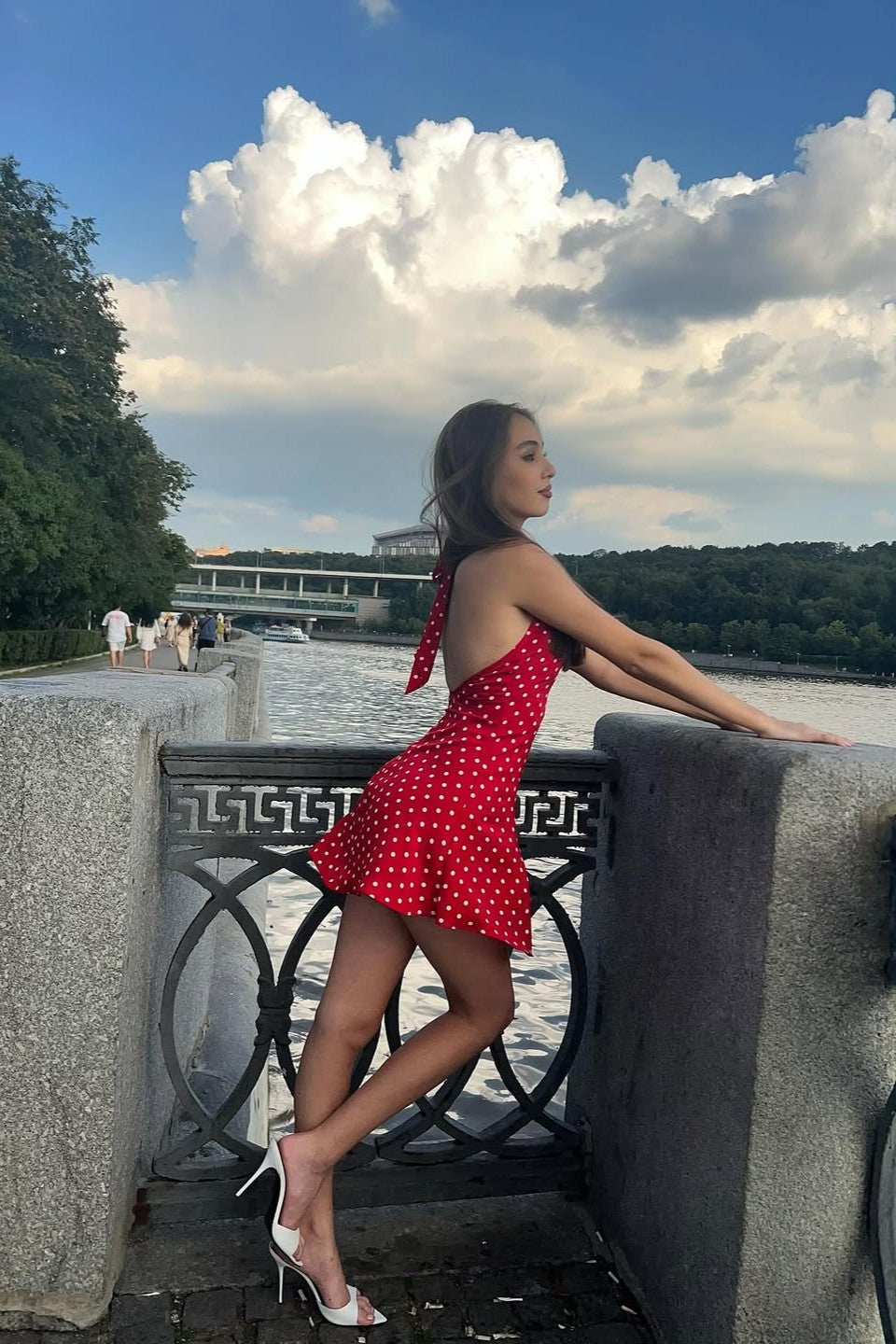 Red polka dot halter mini dress styled with white heels, side pose outdoors