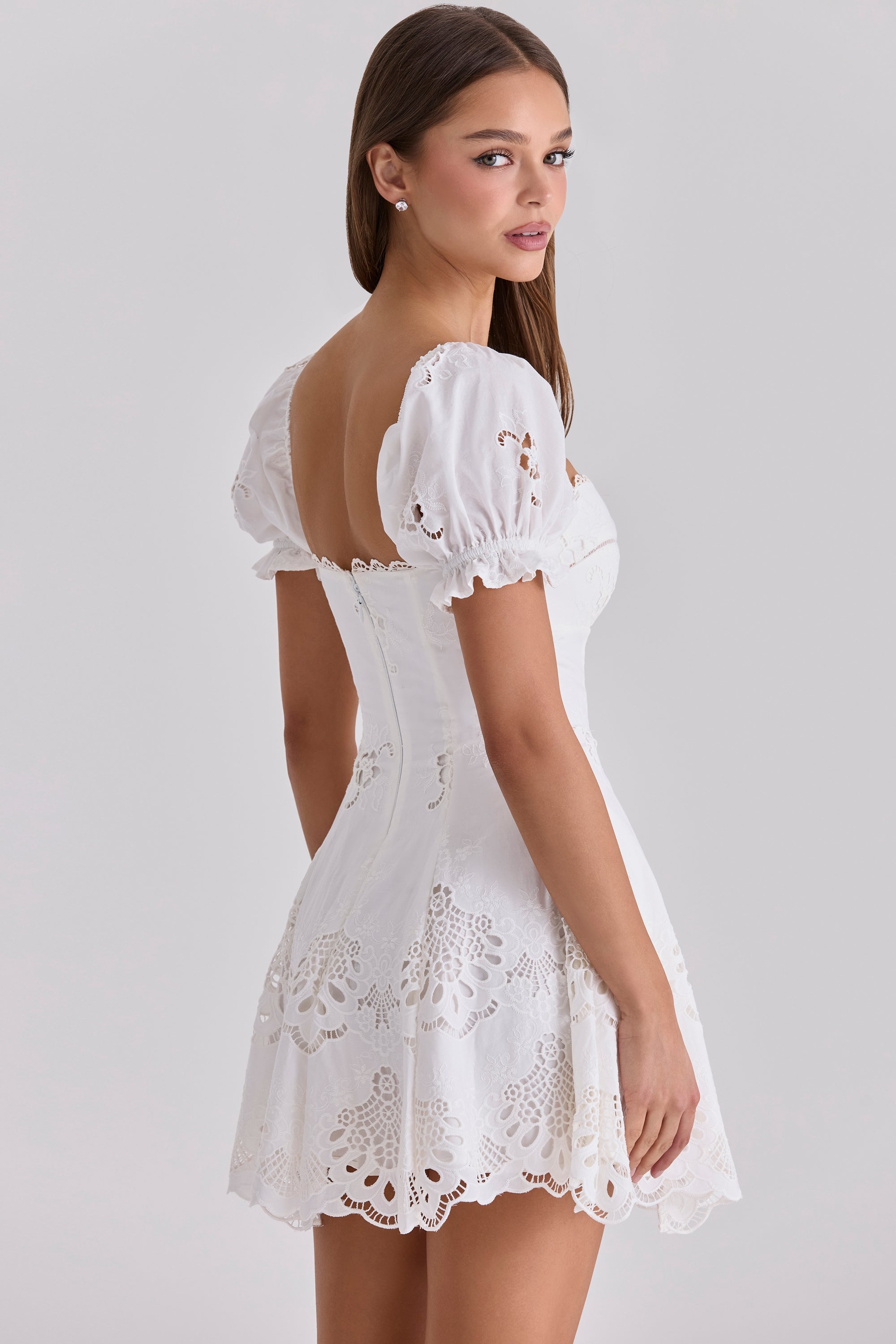 Back three-quarter view of white cotton mini wedding guest dress with puff sleeves and lace hem detail