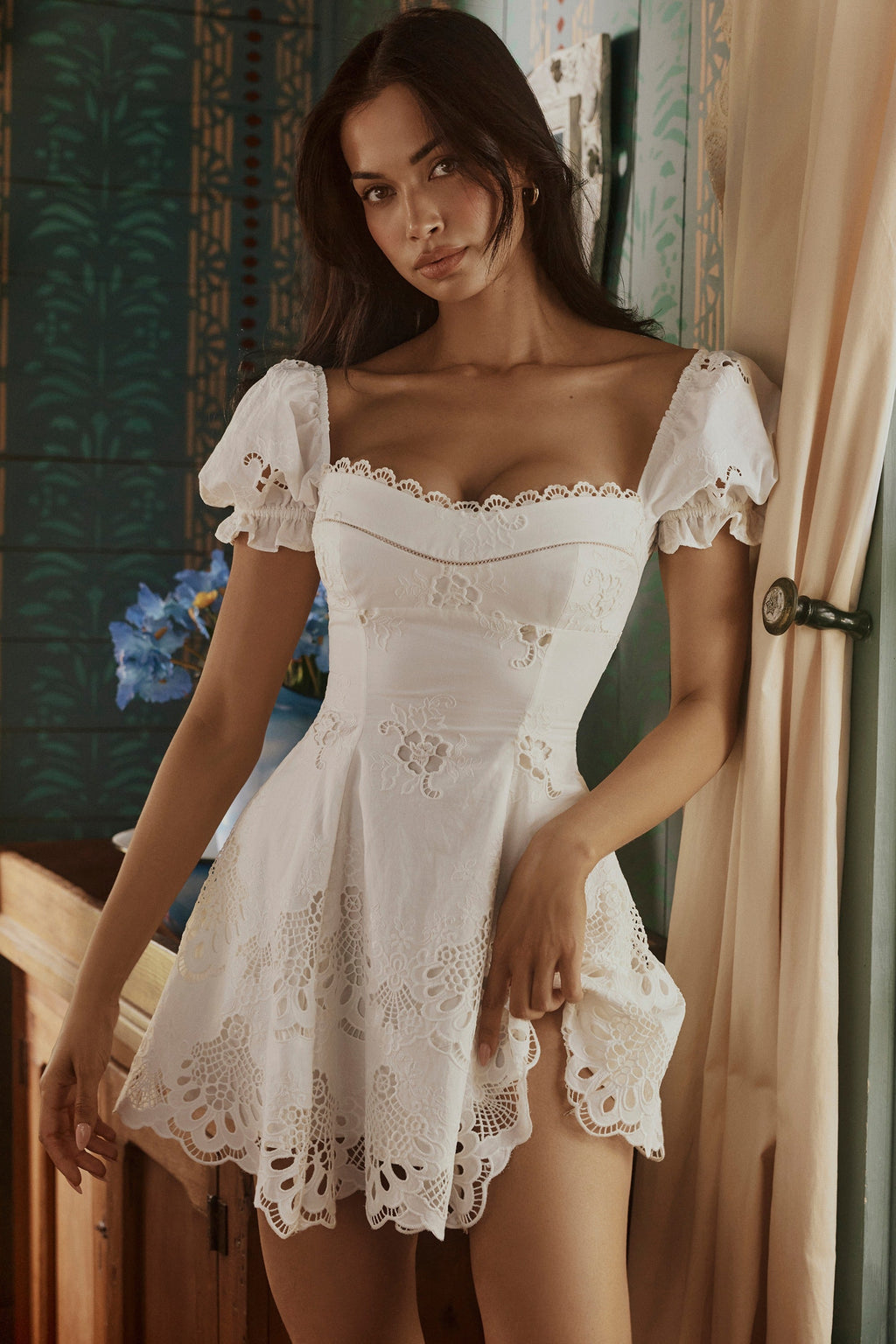 Lifestyle shot of white cotton mini wedding guest dress with embroidered lace and scalloped hem indoors