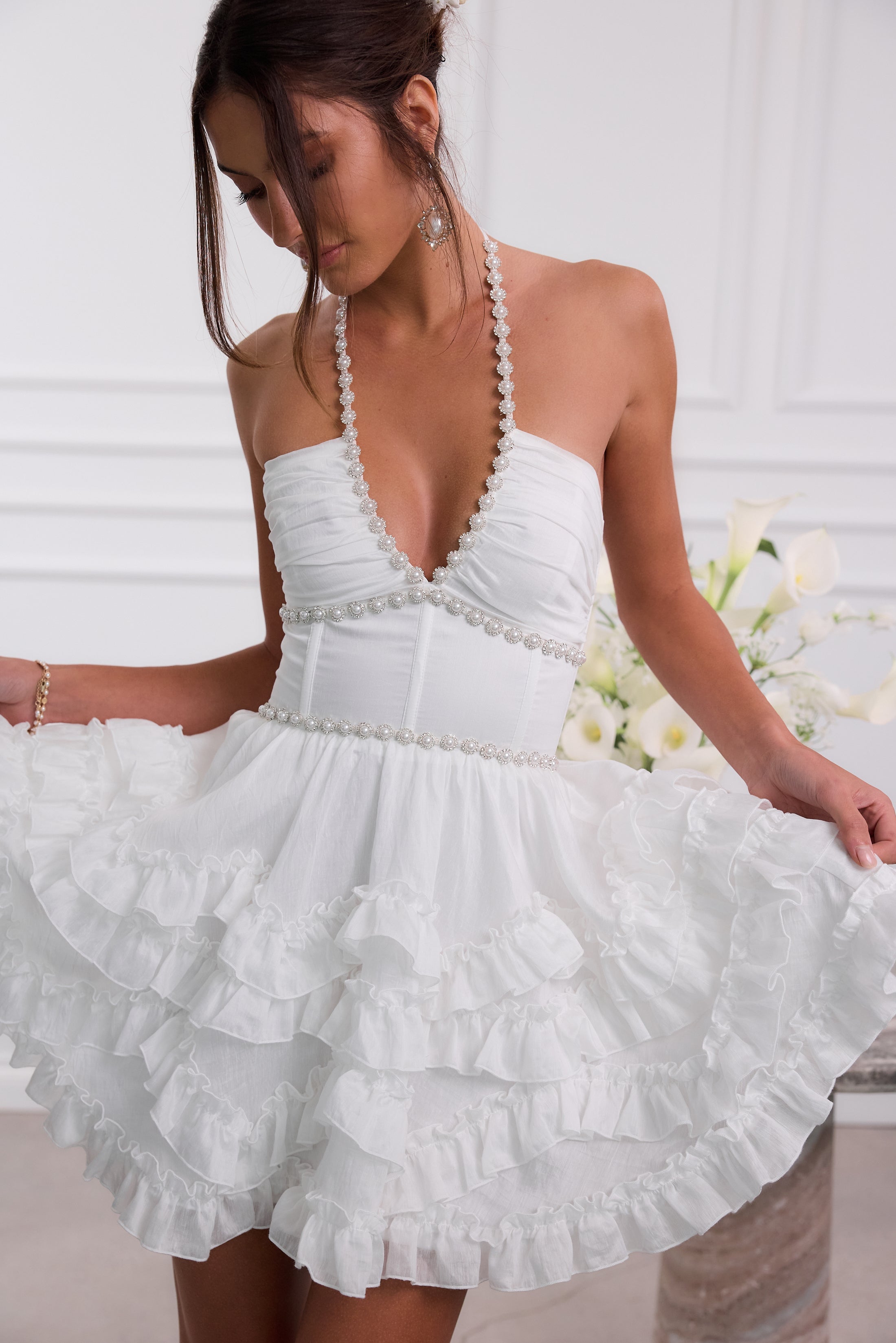 White halter mini dress detail shot with pearl-trim plunge neckline, fitted bodice, and ruffle skirt