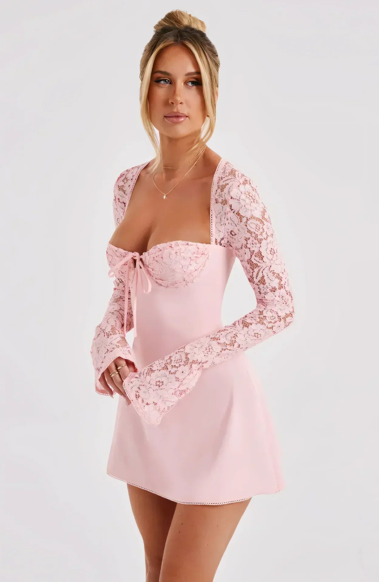 Side view of pink mini dress with sheer lace sleeves and fitted wedding guest silhouette