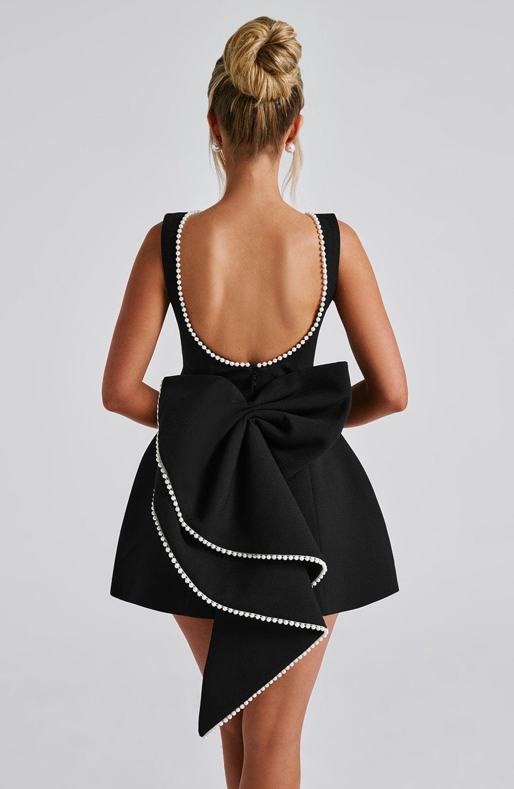 Back view of black pearl neck mini A-line dress with low scoop back and oversized bow with pearl edging