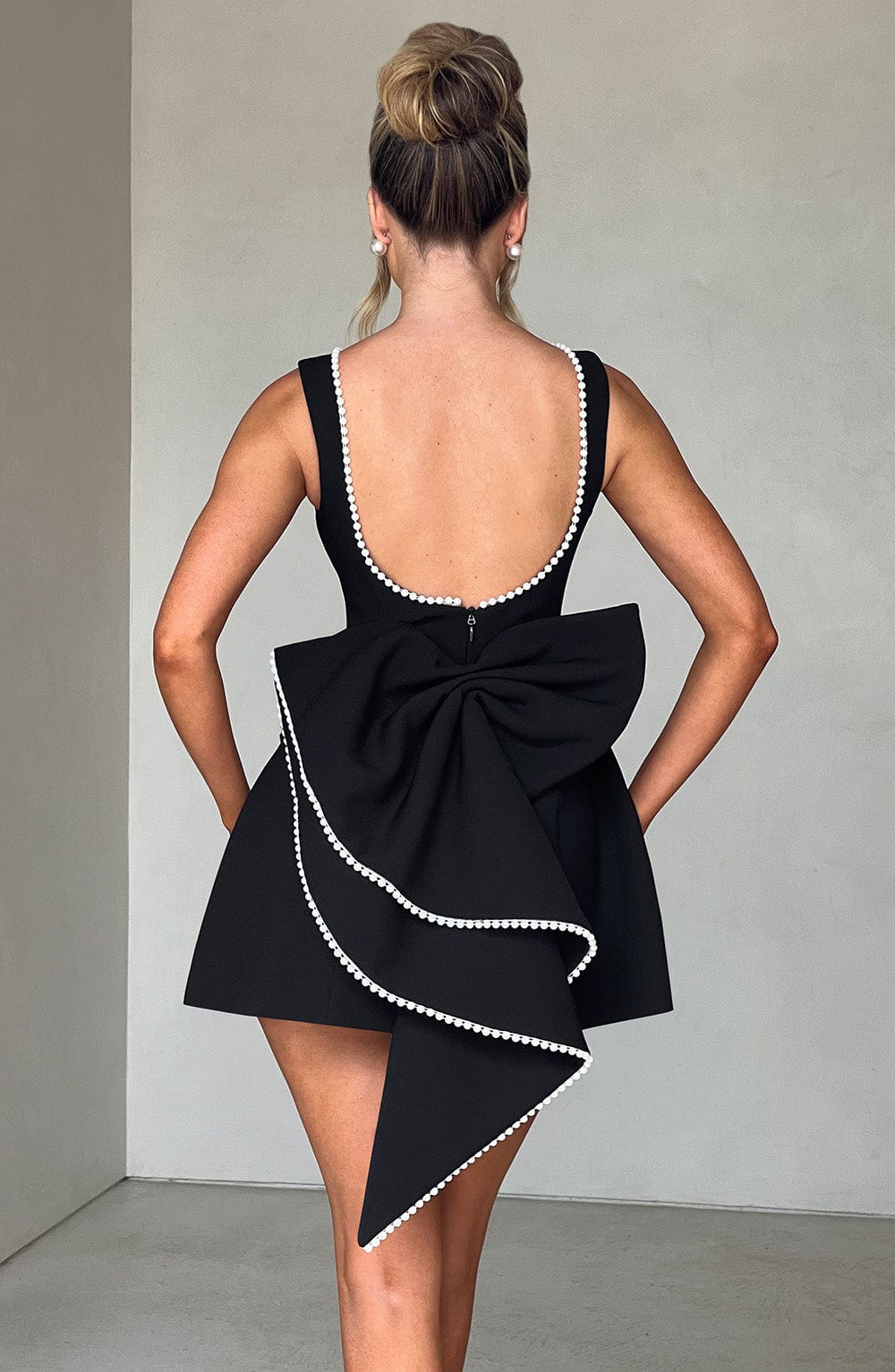 Rear view black pearl neck mini A-line wedding guest dress featuring pearl edged bow and open back