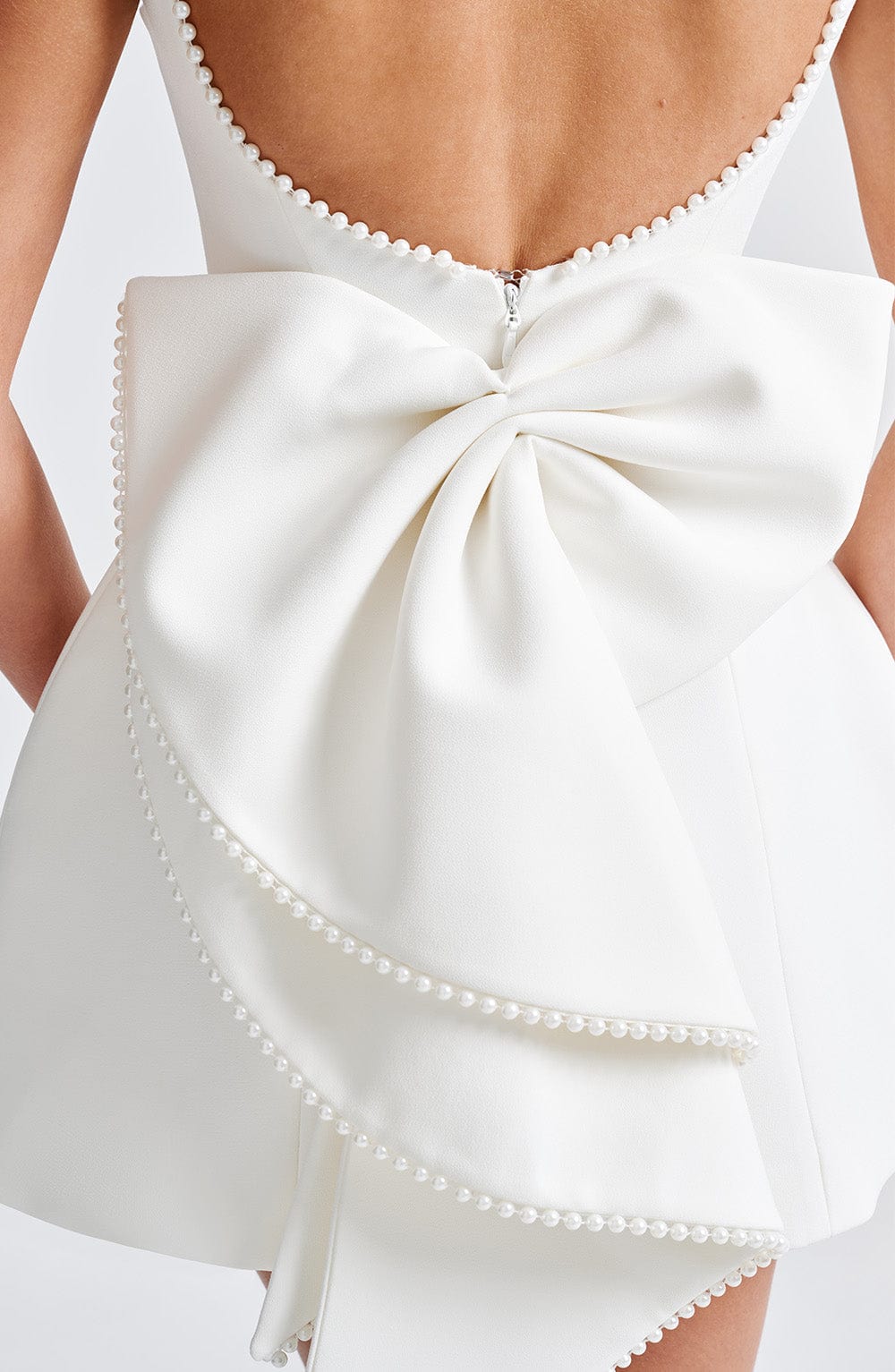 Close-up of oversized bow on white mini A-line dress with pearl edging and back zipper detail