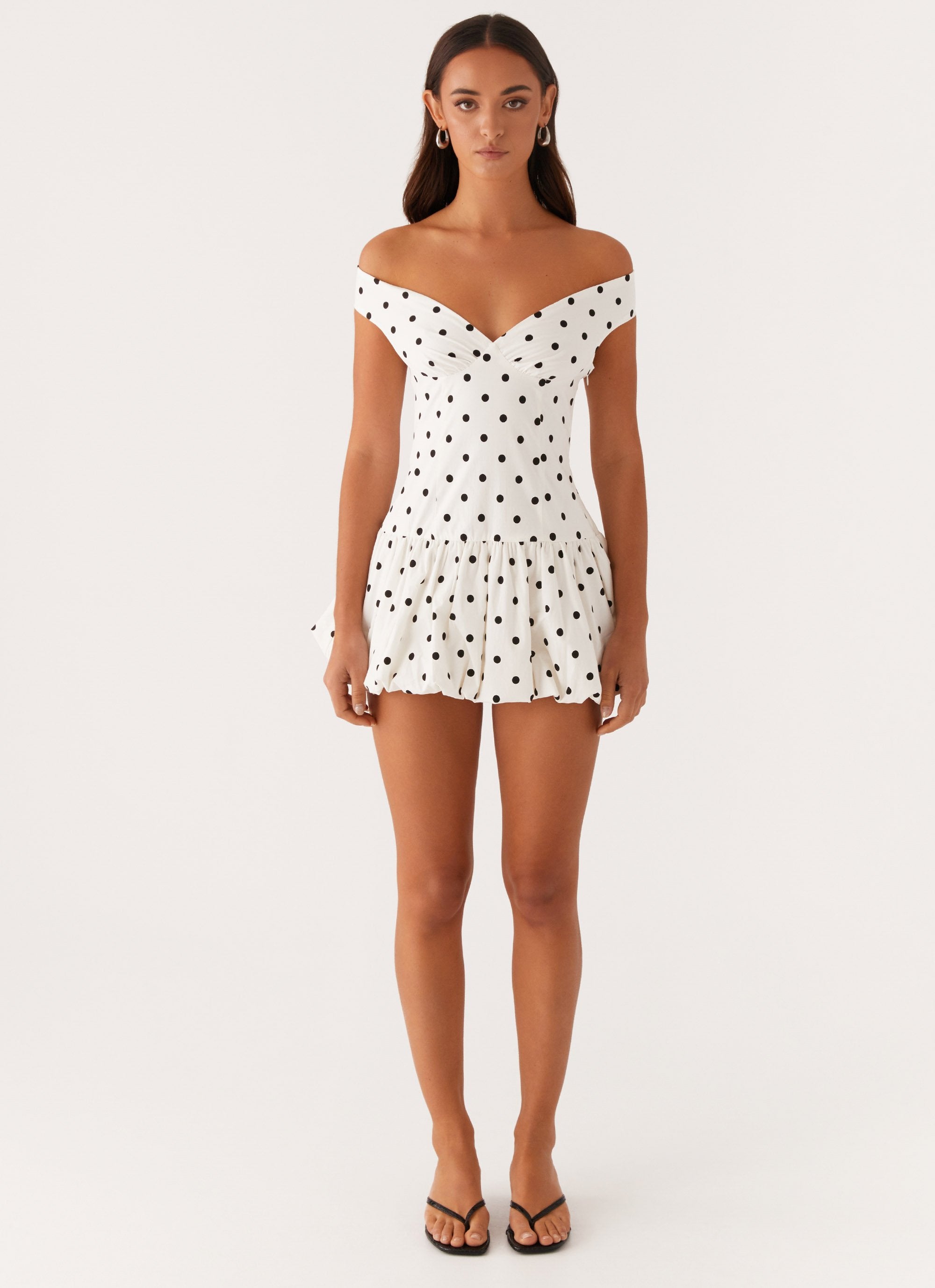 Front full-length view of white polka dot off shoulder mini dress with bubble skirt, wedding guest dress