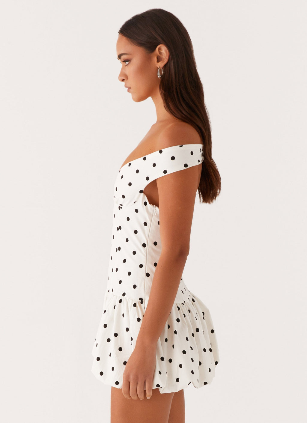 Side profile of white polka dot off shoulder mini dress showing fitted bodice and bubble hem skirt