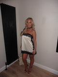 White satin lace mini dress with black trim, thin straps, and strappy black heels