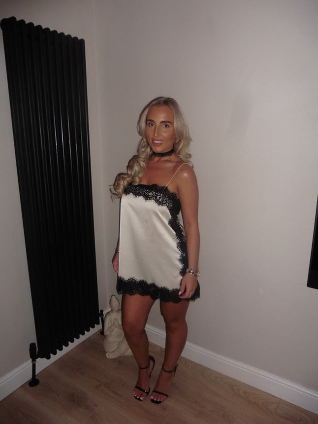 White satin lace mini dress with black trim, thin straps, and strappy black heels