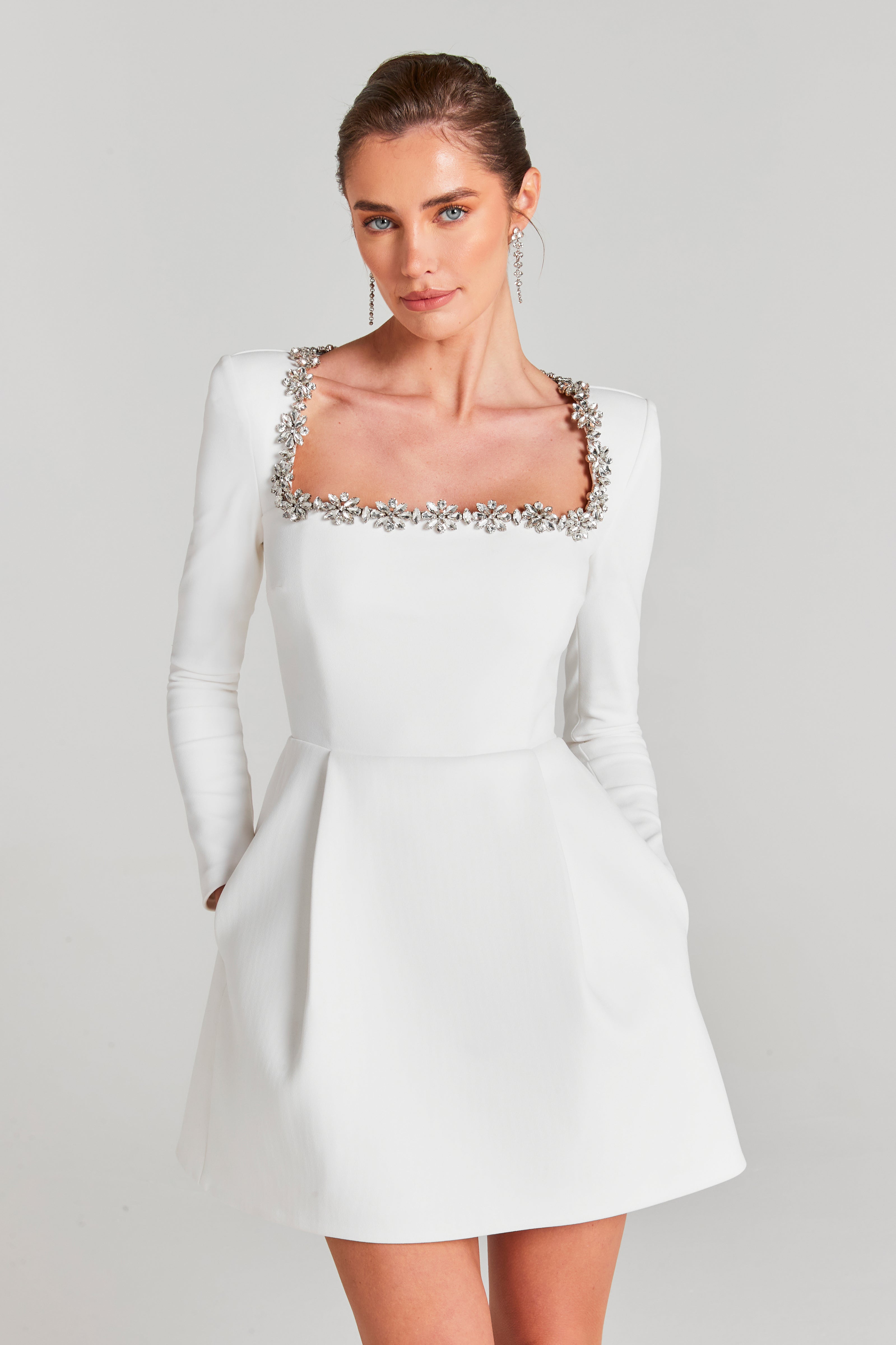 Close-up of white velvet wedding guest dress with jeweled square neckline and fitted sleeves