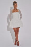 White mini dress with square neckline, sheer long sleeves, and sparkling sequin finish