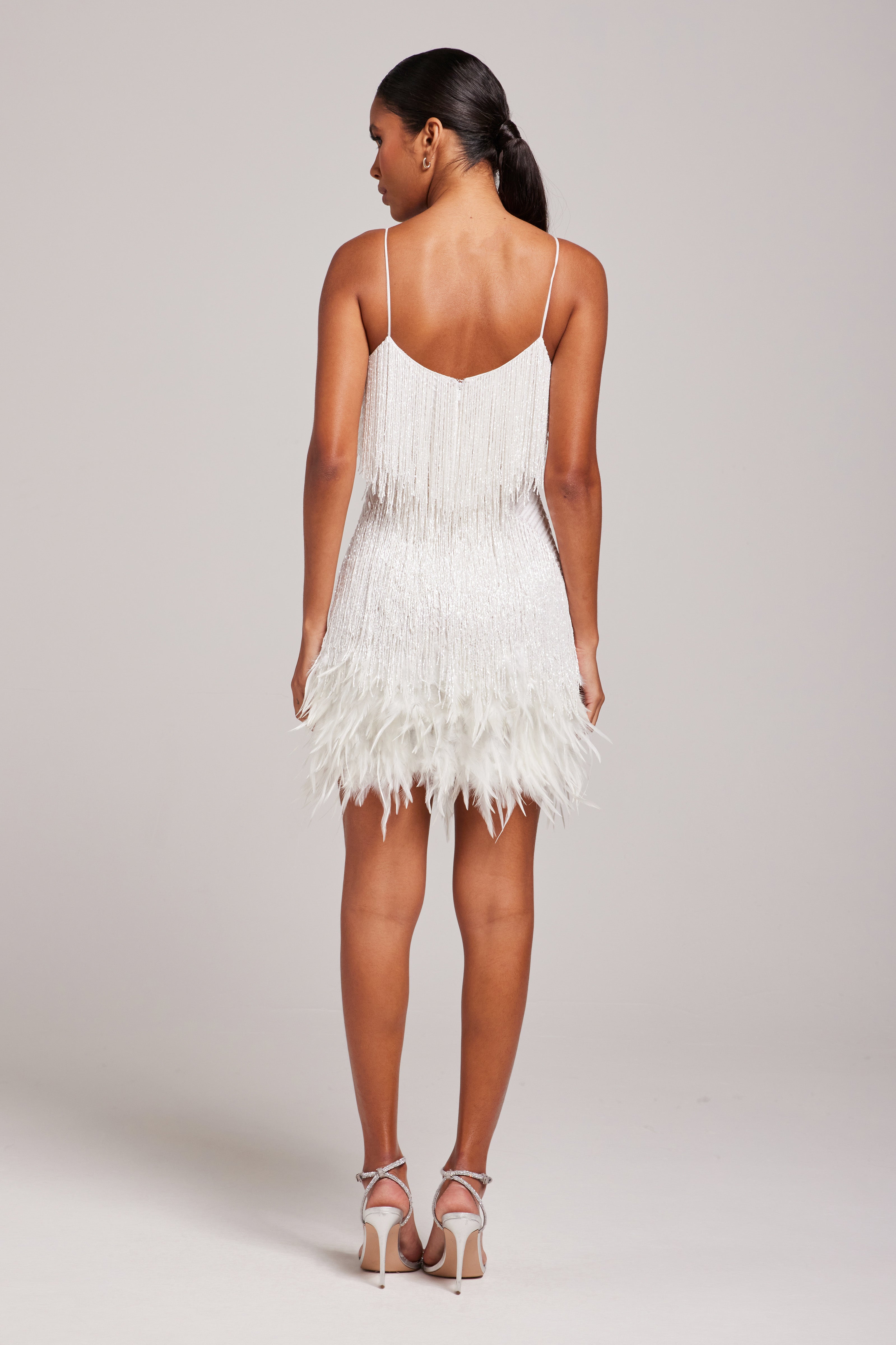 Back view of white fringe mini dress with open back, thin straps, and feather hem